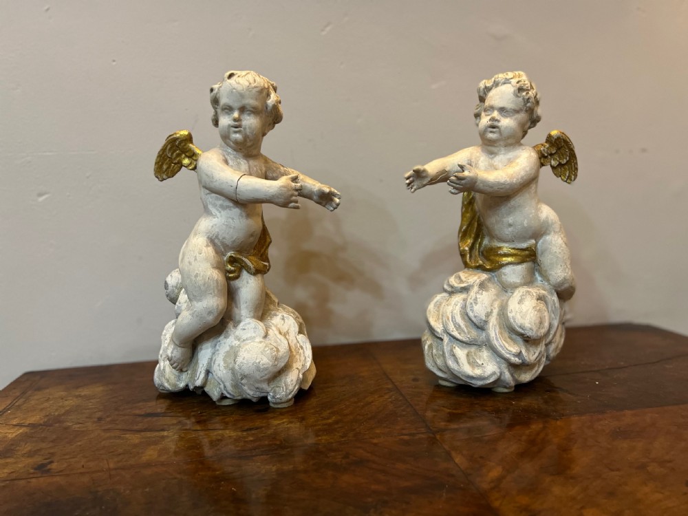 A pair of 18th-century carved wood polychrome putti featuring painted off-white figures with gilded wings and drapery, resting upon carved cloud bases. View XII