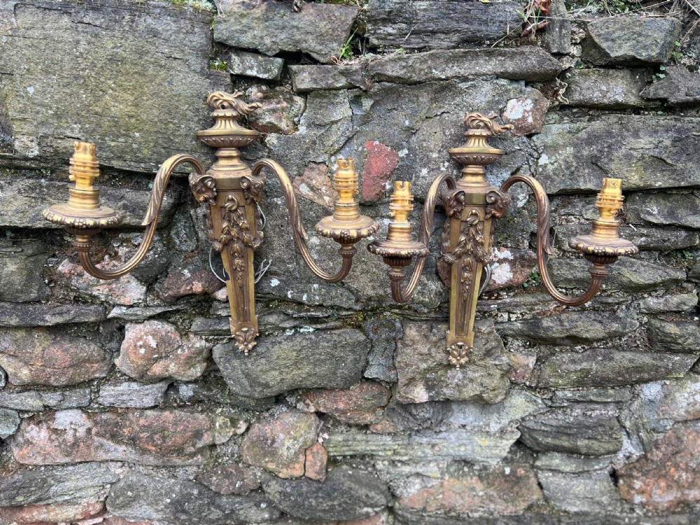 A pair of Edwardian cast brass twin-arm wall lights designed in the Neoclassical Adam style with urn finials and tapered backplates. View IV