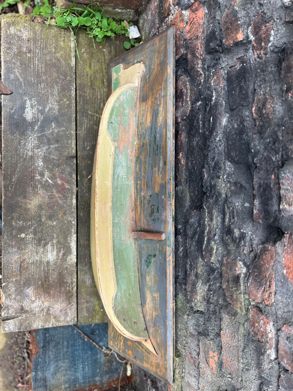 A carved wooden half-hull boat model with cream and green painted finish, mounted on a rectangular blue wooden backboard. View III