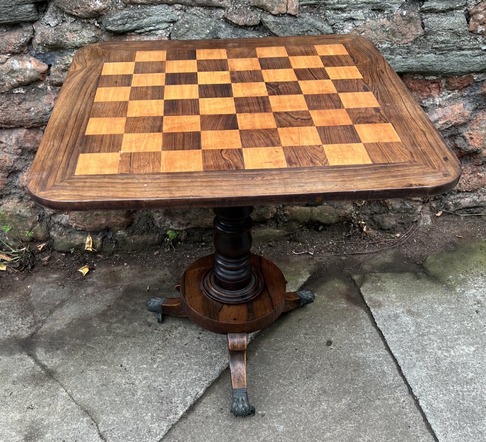 An antique Regency rosewood occasional table featuring an inlaid satinwood and rosewood chequered top over a turned pedestal and brass paw feet.