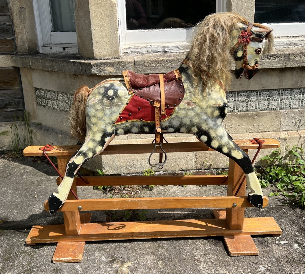 A vintage carved wooden Collinson rocking horse featuring a dapple grey painted finish, natural horsehair mane, red corduroy saddle, and leather tack on a wooden safety stand.