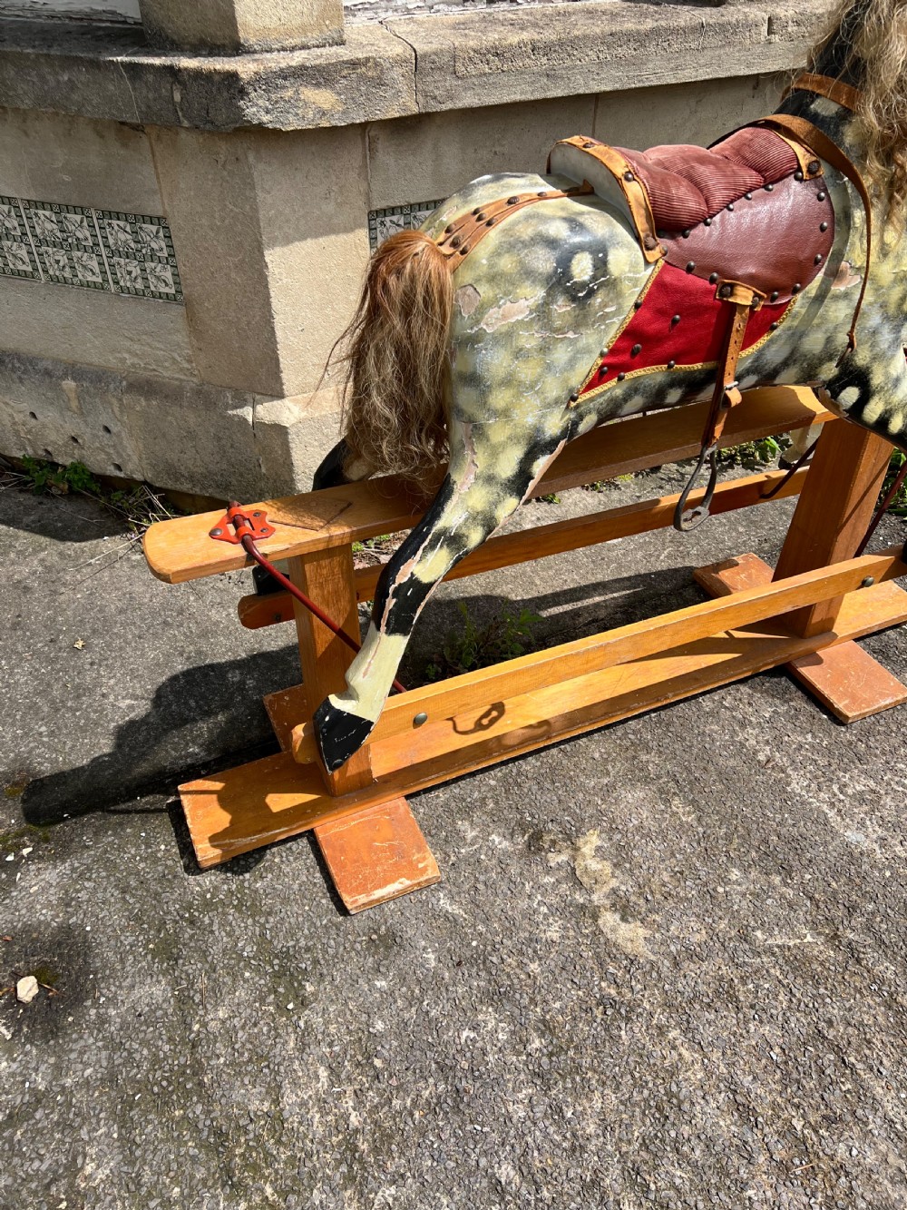A vintage carved wooden Collinson rocking horse featuring a dapple grey painted finish, natural horsehair mane, red corduroy saddle, and leather tack on a wooden safety stand. View VII