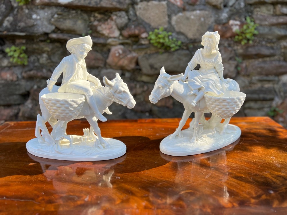 Pair of porcelain figures by moore bros, depicting a man and a woman riding donkeys 