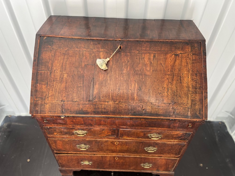 An early eighteenth-century walnut slant-front bureau featuring graduated drawers, brass drop handles, and bracket feet. View VI