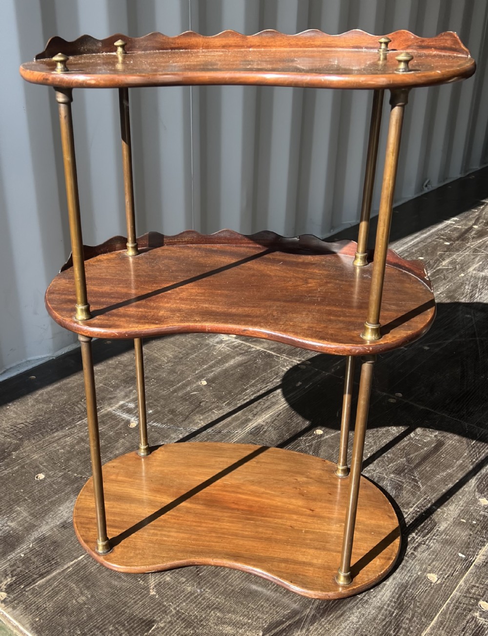 A 19th-century three-tiered mahogany kidney-shaped washstand supported by polished brass upright columns and topped with a gallery edge.