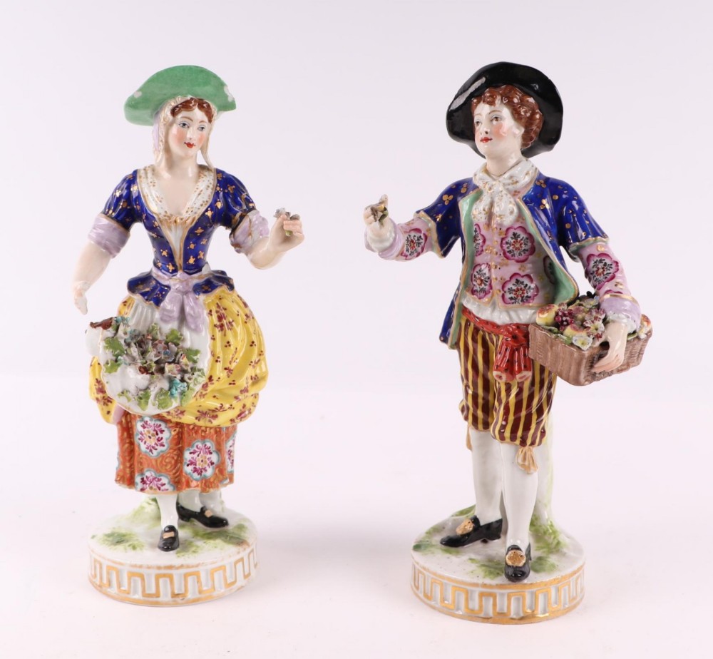 A pair of 18th-century Derby porcelain figures depicting a man and woman in colourful Georgian attire holding baskets of flowers, mounted on circular gilded bases.