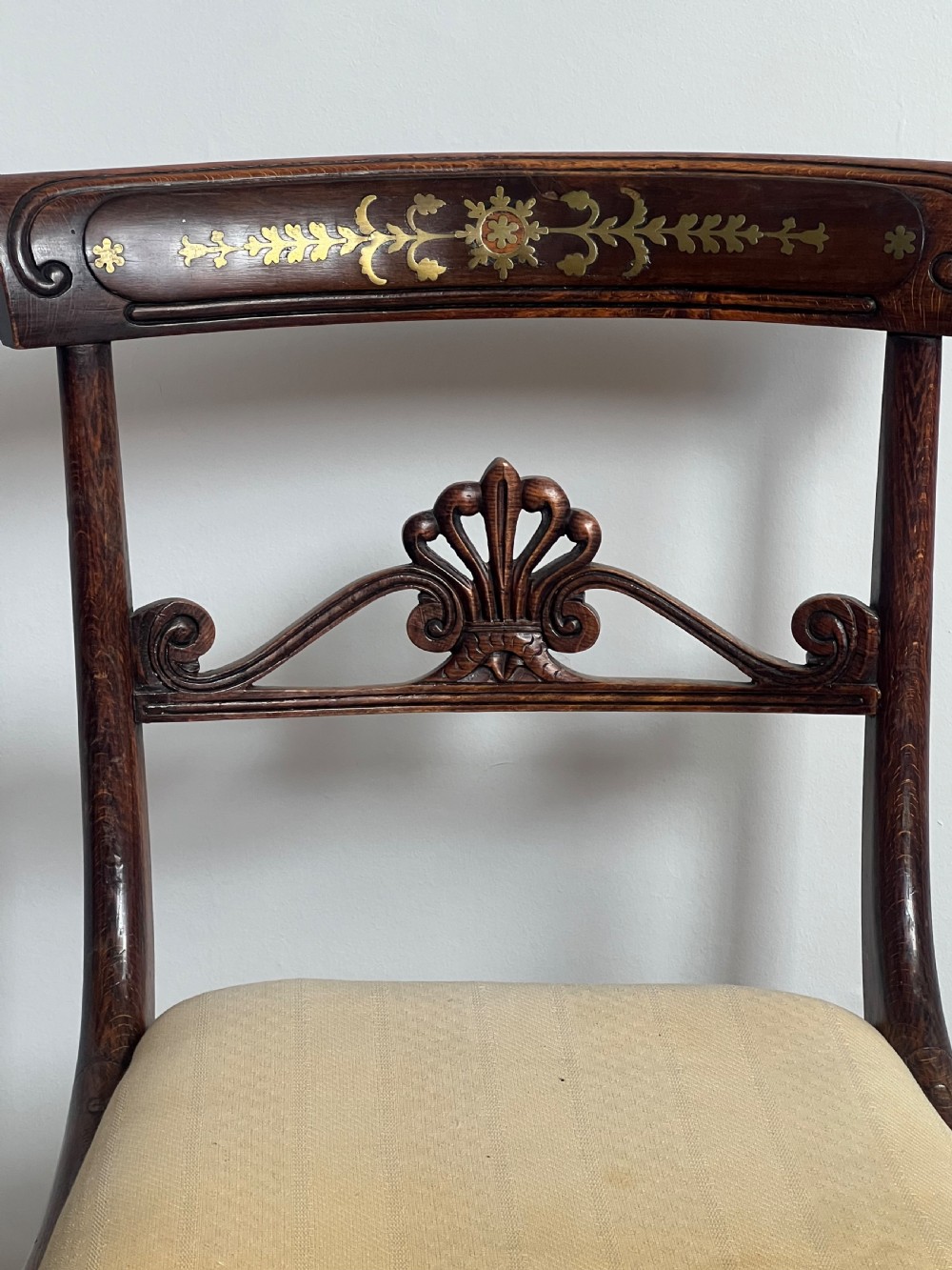 A pair of Regency faux rosewood side chairs featuring brass inlaid crest rails, carved anthemion splats, sabre legs, and pale yellow upholstered seats. View II