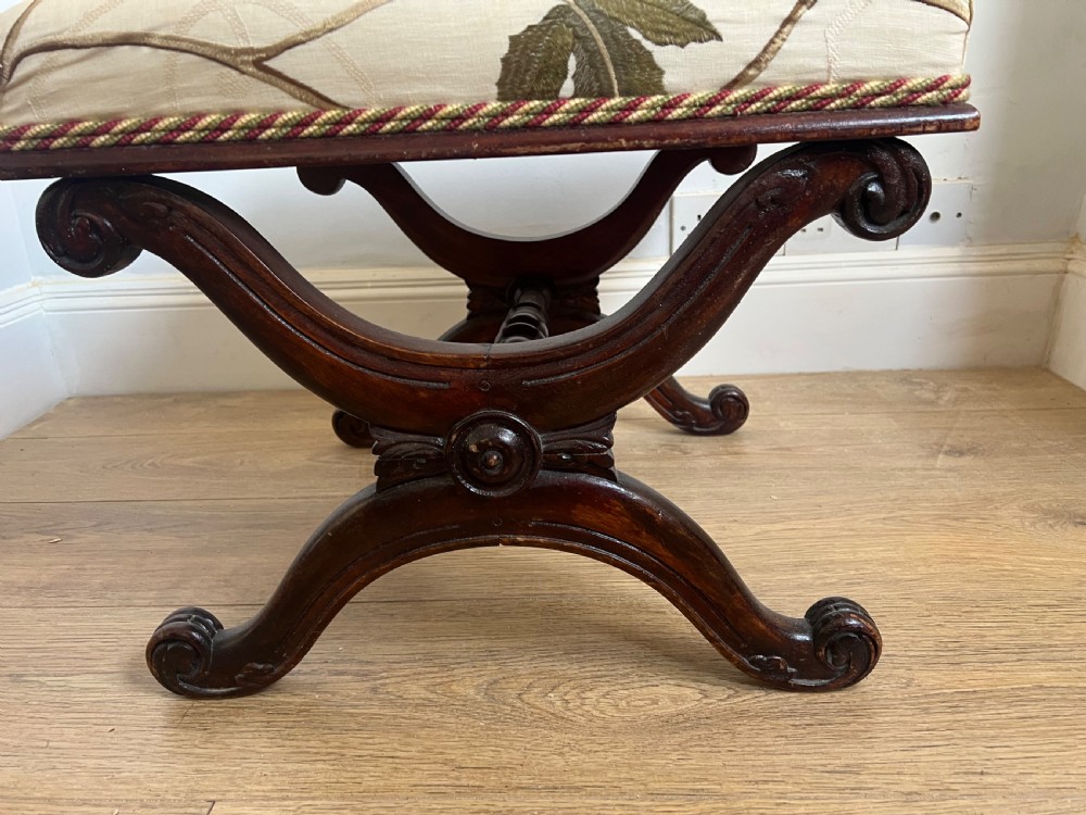 A 19th-century mahogany X-frame stool featuring carved scroll legs, a turned central stretcher, and a cream floral embroidered upholstered cushion. View II