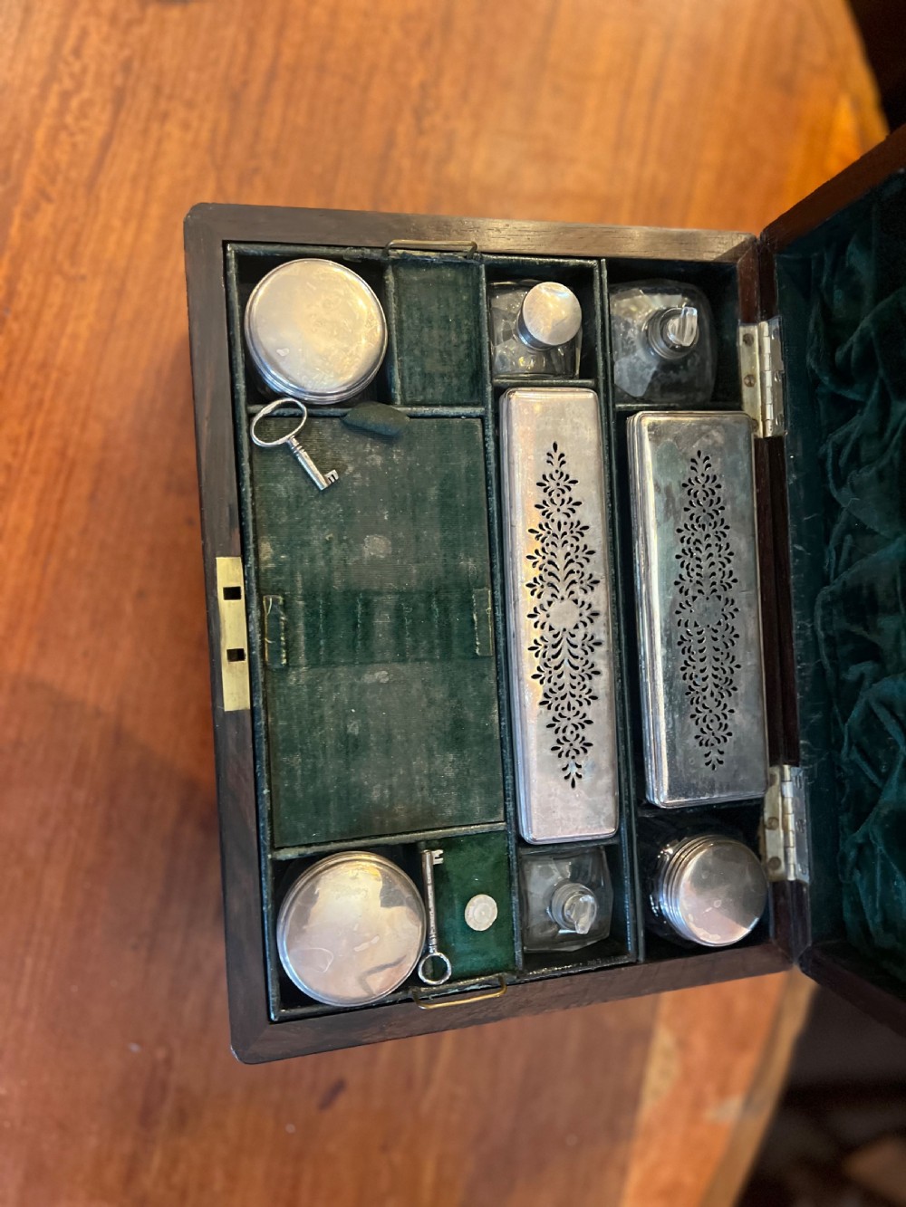 An open Victorian rosewood workbox featuring floral mother of pearl inlay, fitted green velvet interior, silver-toned vanity jars, glass bottles, and two small keys. View III