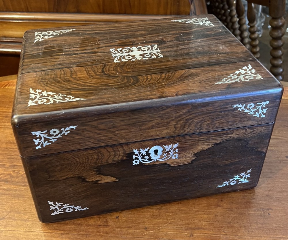 An open Victorian rosewood workbox featuring floral mother of pearl inlay, fitted green velvet interior, silver-toned vanity jars, glass bottles, and two small keys. View VI