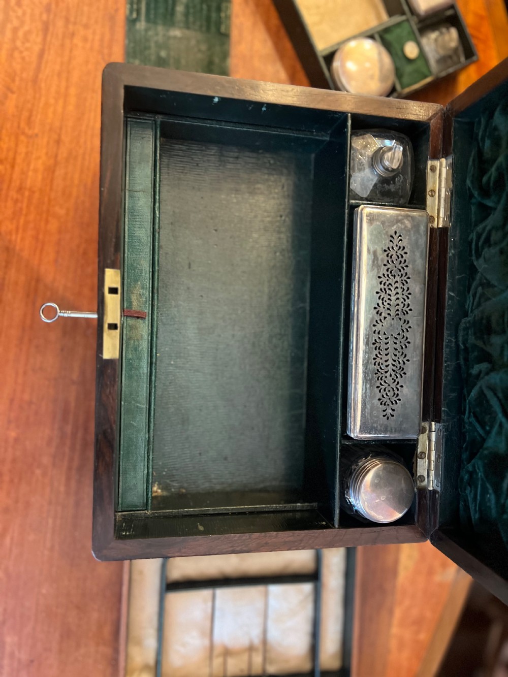 An open Victorian rosewood workbox featuring floral mother of pearl inlay, fitted green velvet interior, silver-toned vanity jars, glass bottles, and two small keys. View X