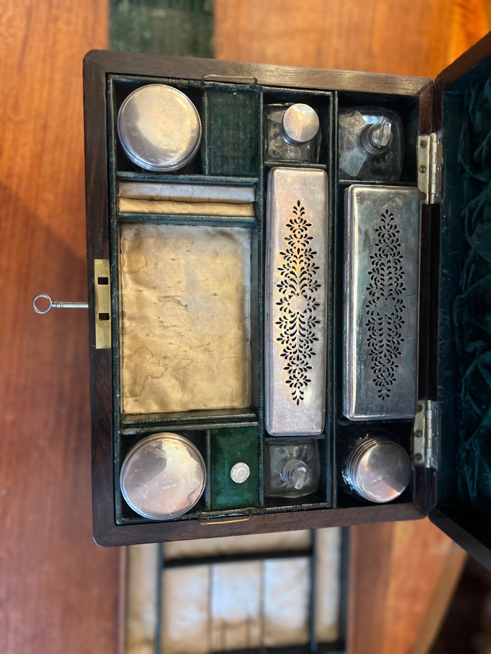 An open Victorian rosewood workbox featuring floral mother of pearl inlay, fitted green velvet interior, silver-toned vanity jars, glass bottles, and two small keys. View XII