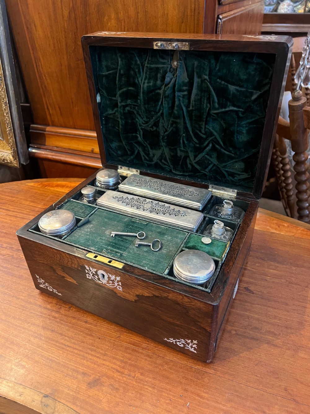 An open Victorian rosewood workbox featuring floral mother of pearl inlay, fitted green velvet interior, silver-toned vanity jars, glass bottles, and two small keys. View XVII