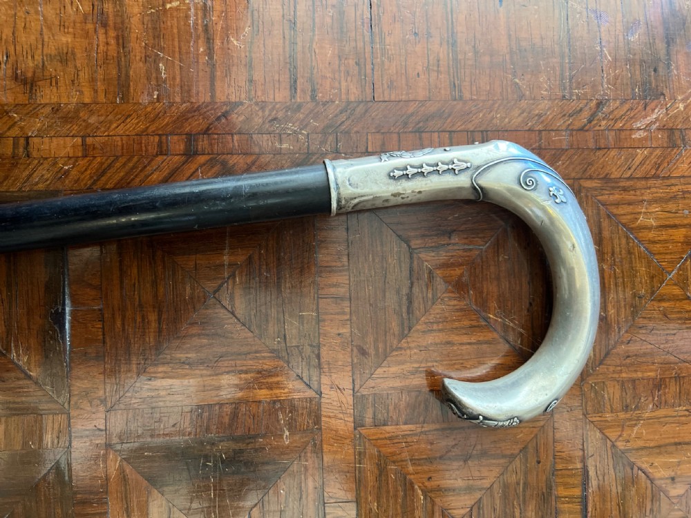 An antique walking stick featuring an embossed silver crook handle attached to a polished black wooden shaft.