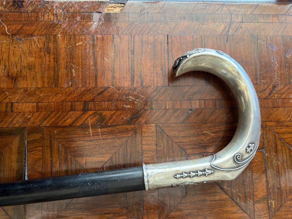 An antique walking stick featuring an embossed silver crook handle attached to a polished black wooden shaft. View II