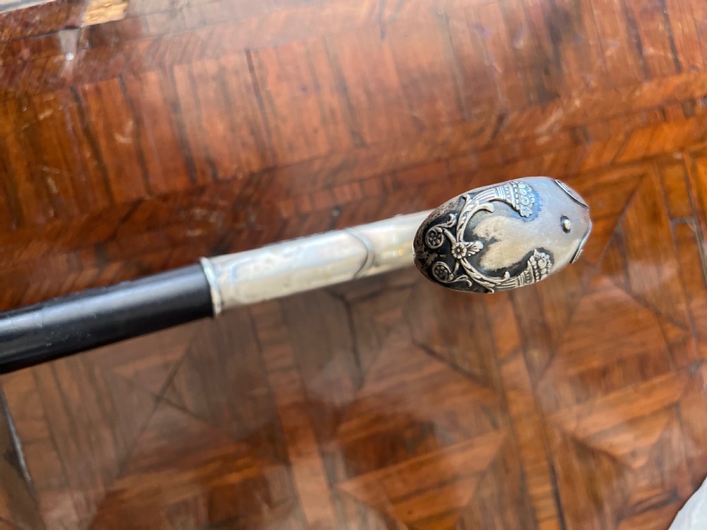 An antique walking stick featuring an embossed silver crook handle attached to a polished black wooden shaft. View III