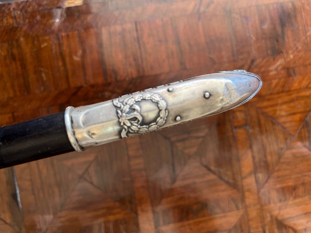 An antique walking stick featuring an embossed silver crook handle attached to a polished black wooden shaft. View IV