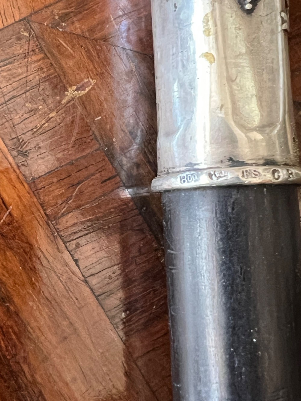 An antique walking stick featuring an embossed silver crook handle attached to a polished black wooden shaft. View VI