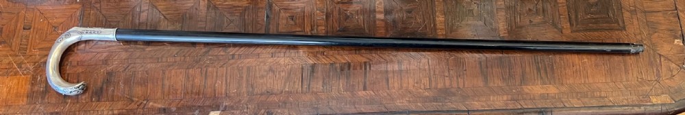An antique walking stick featuring an embossed silver crook handle attached to a polished black wooden shaft. View VII