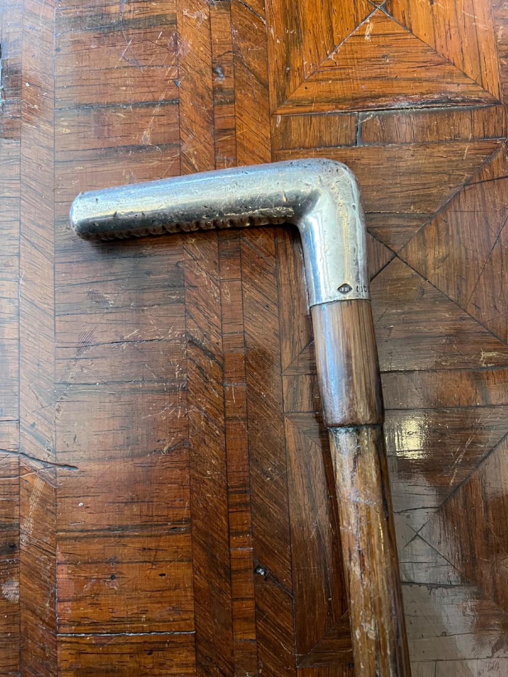 A hallmarked silver L-shaped handle mounted on a linear-grained palm wood walking stick shaft.