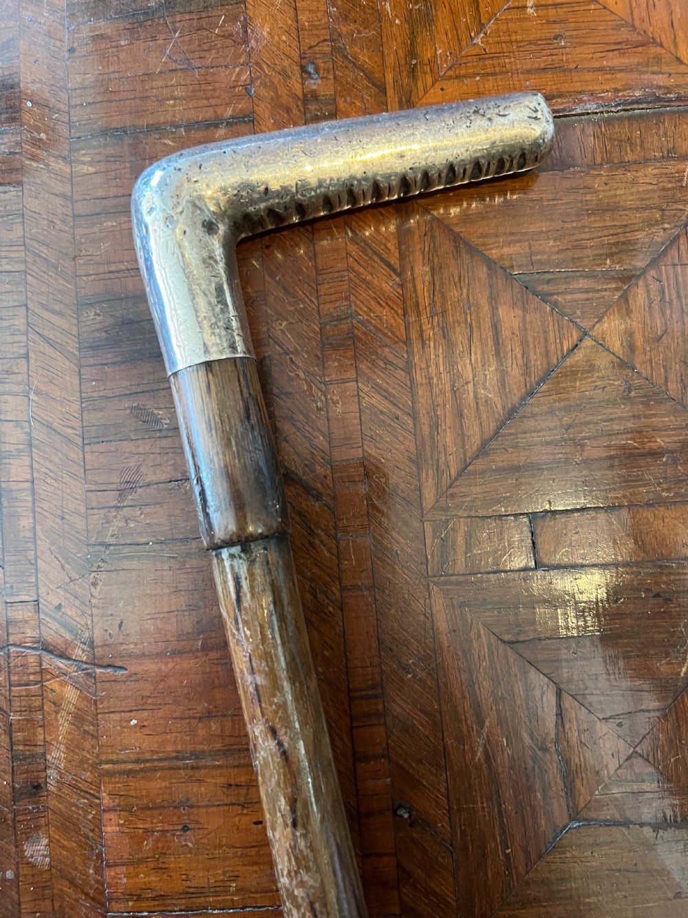 A hallmarked silver L-shaped handle mounted on a linear-grained palm wood walking stick shaft. View II