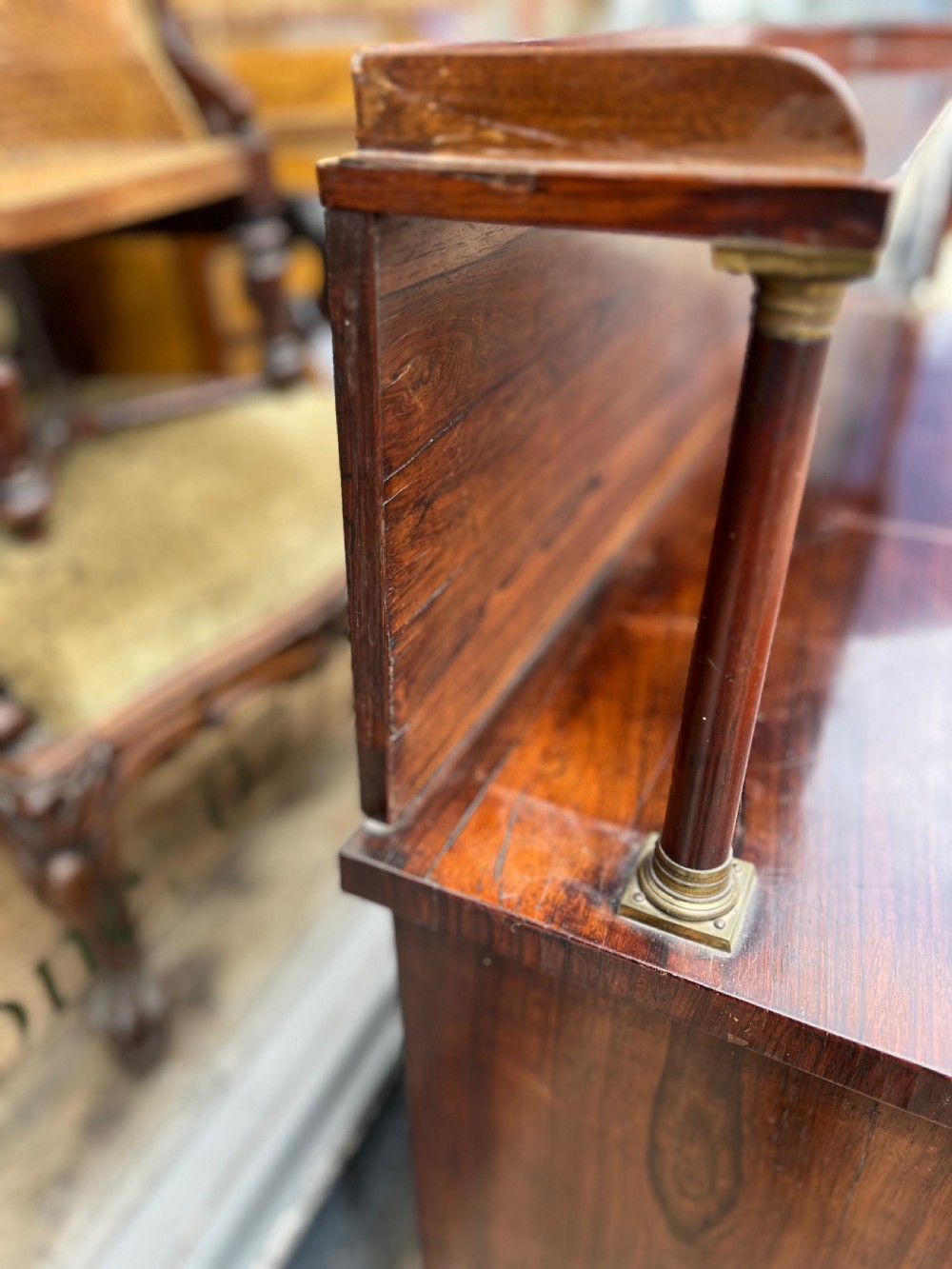 An antique Regency dark rosewood side cabinet featuring brass floral inlay, twin panelled doors, side columns with brass capitals, and an upper shelf resting on turned brass pillars. View VII