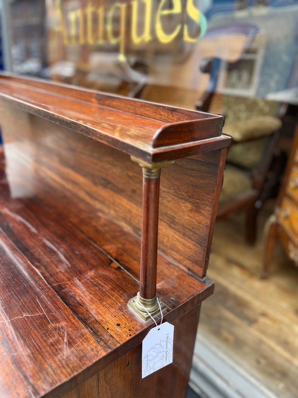 An antique Regency dark rosewood side cabinet featuring brass floral inlay, twin panelled doors, side columns with brass capitals, and an upper shelf resting on turned brass pillars. View VIII