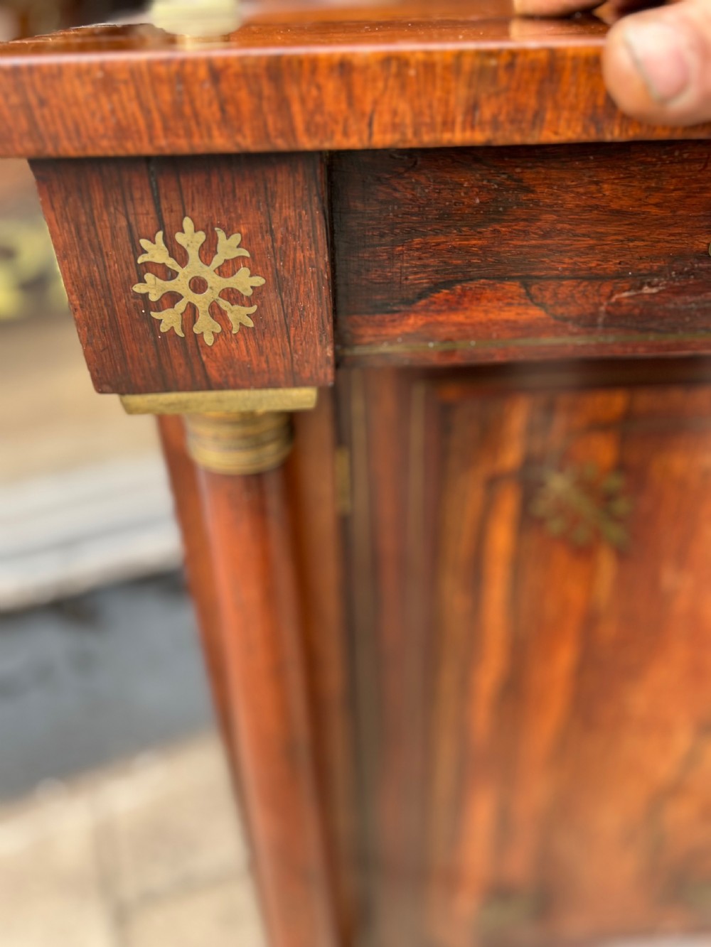 An antique Regency dark rosewood side cabinet featuring brass floral inlay, twin panelled doors, side columns with brass capitals, and an upper shelf resting on turned brass pillars. View XII