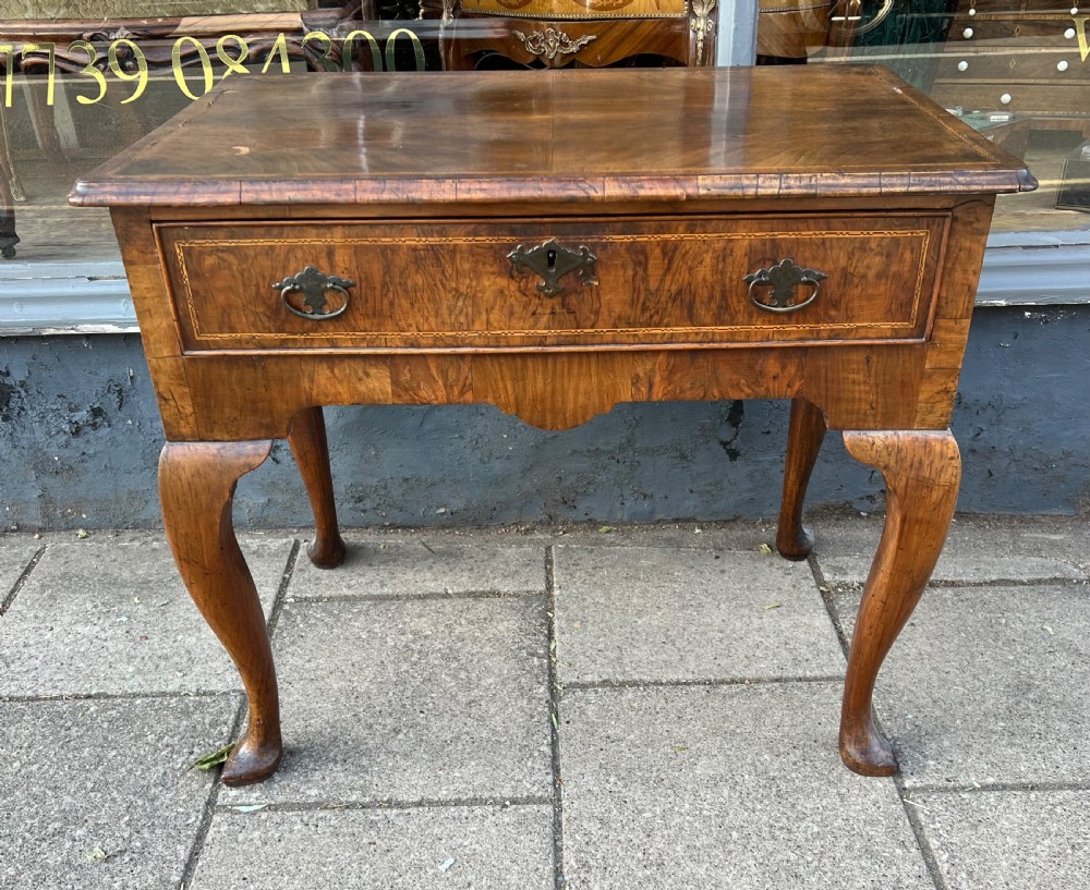 An early Georgian walnut side table with a single drawer, brass handles, shaped apron, and four cabriole legs.