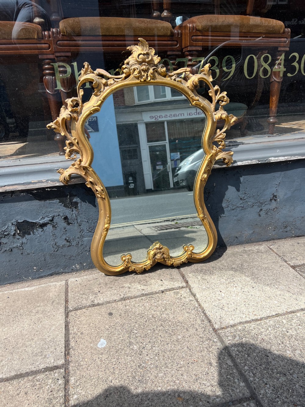 An ornate Rococo style wall mirror with a carved giltwood frame featuring elaborate acanthus leaf scrolls and a top cresting. View II