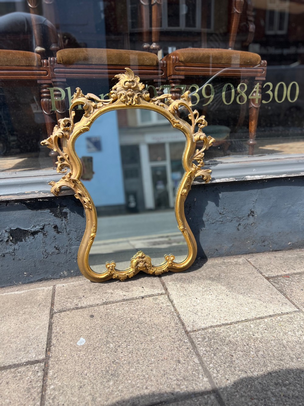 An ornate Rococo style wall mirror with a carved giltwood frame featuring elaborate acanthus leaf scrolls and a top cresting. View III