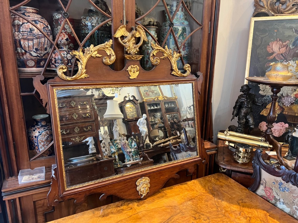 An Edwardian mahogany fretwork wall mirror featuring an ornate parcel gilt eagle finial and classical mask motif.