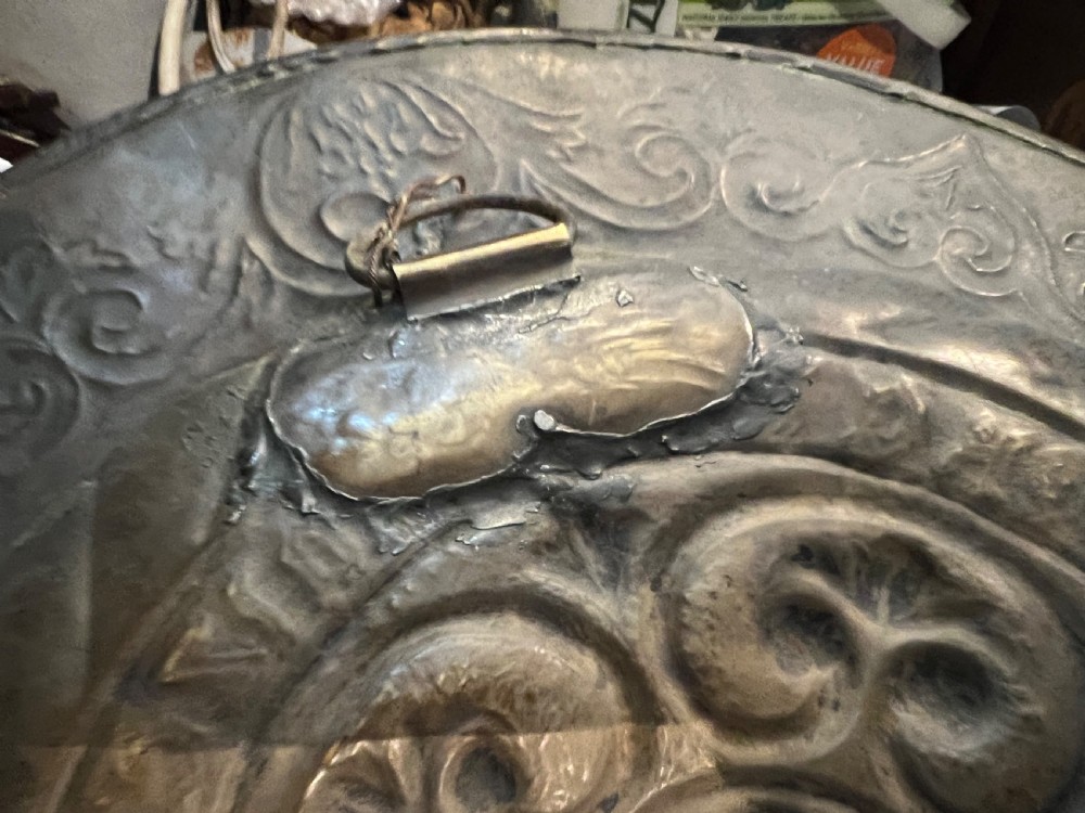 A circular 18th-century brass alms dish featuring an embossed central floral boss, a ring of gothic lettering, and a foliate patterned rim. View III