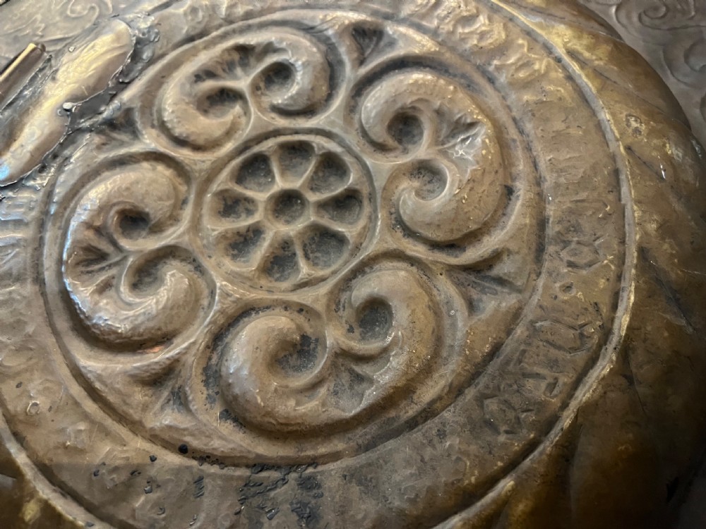 A circular 18th-century brass alms dish featuring an embossed central floral boss, a ring of gothic lettering, and a foliate patterned rim. View VII