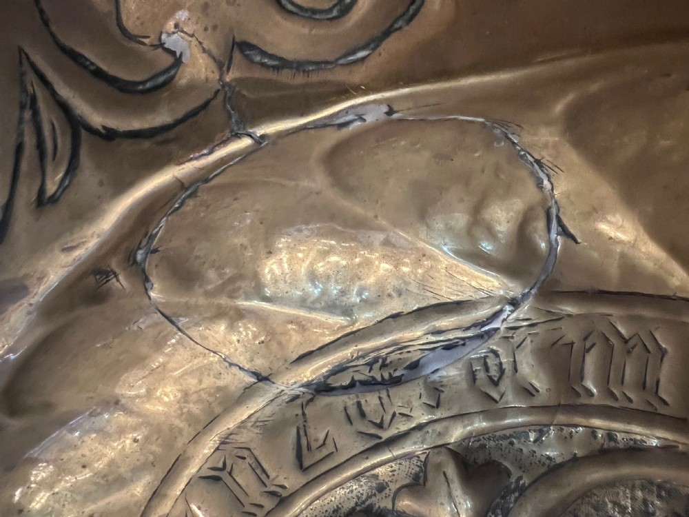 A circular 18th-century brass alms dish featuring an embossed central floral boss, a ring of gothic lettering, and a foliate patterned rim. View VIII