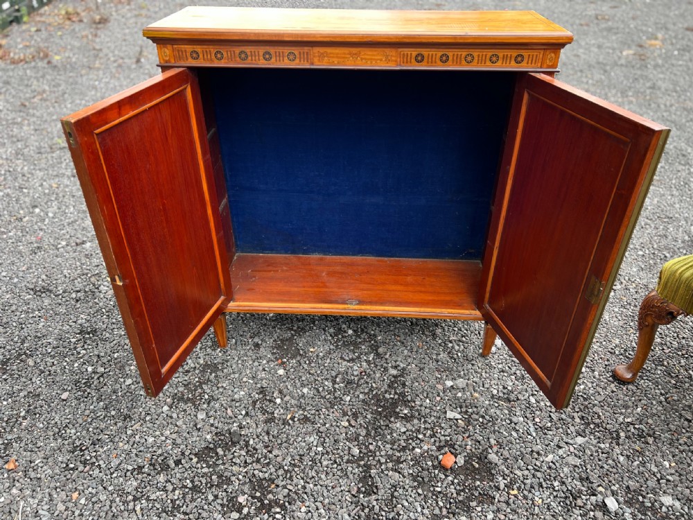 A satinwood side cabinet featuring two cupboard doors with central marquetry urn inlays, a decorated top frieze, and square tapered feet. View VI