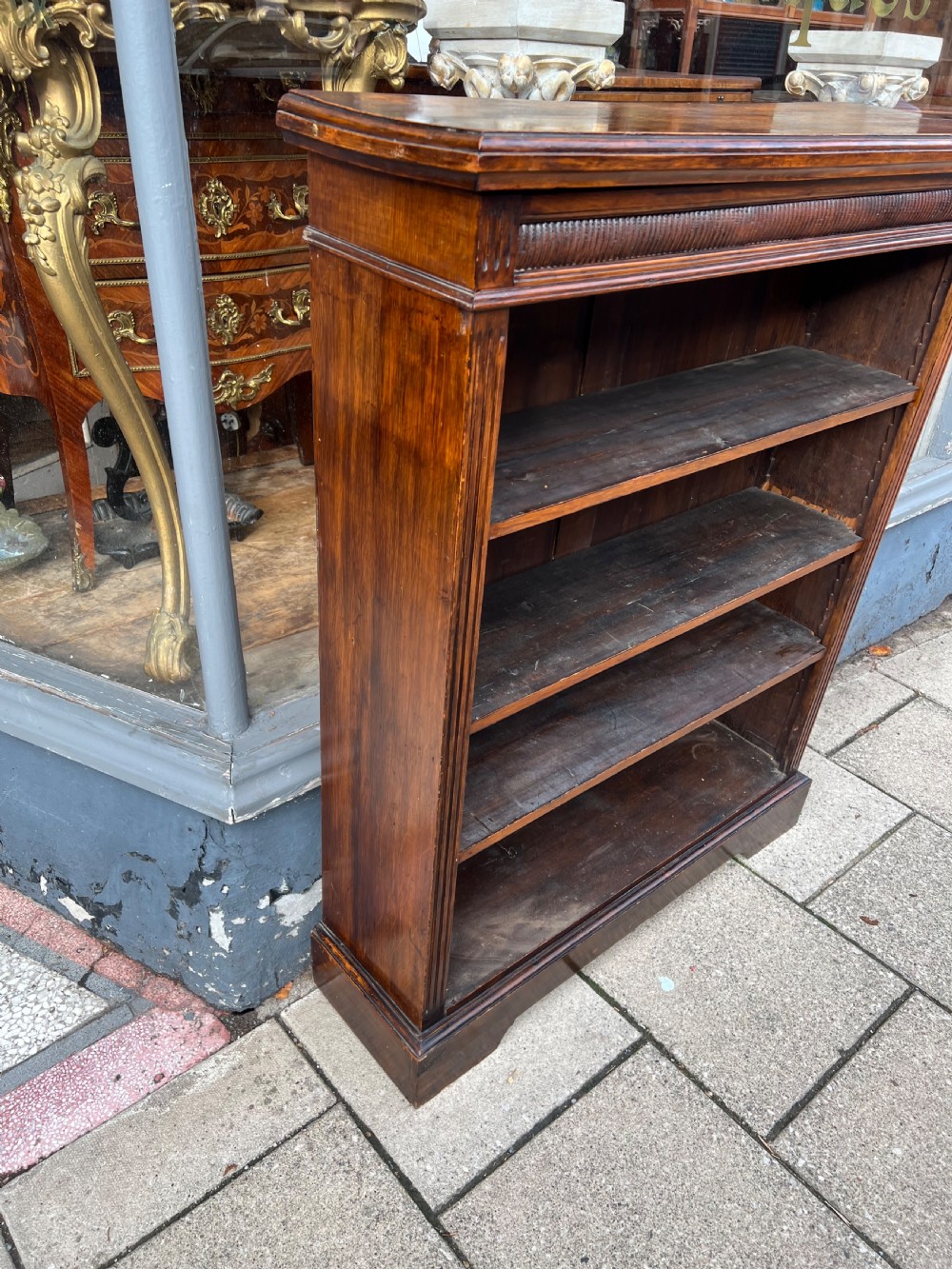 An antique open Edwardian oak bookcase featuring four storage levels, fluted side pilasters, and a carved frieze above a solid plinth base. View II