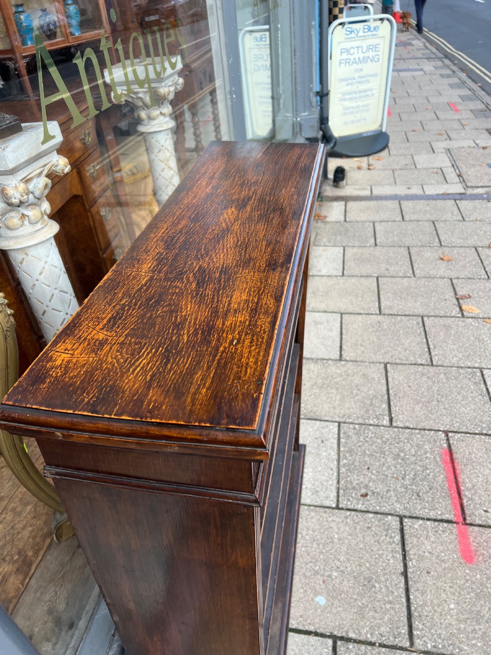 An antique open Edwardian oak bookcase featuring four storage levels, fluted side pilasters, and a carved frieze above a solid plinth base. View III