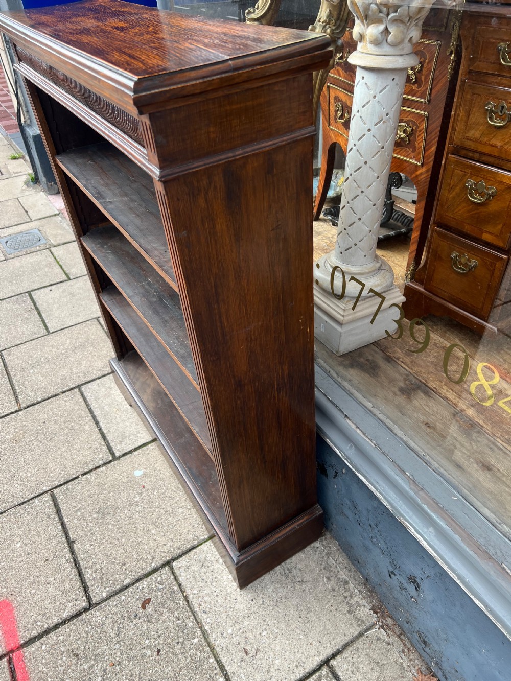 An antique open Edwardian oak bookcase featuring four storage levels, fluted side pilasters, and a carved frieze above a solid plinth base. View V