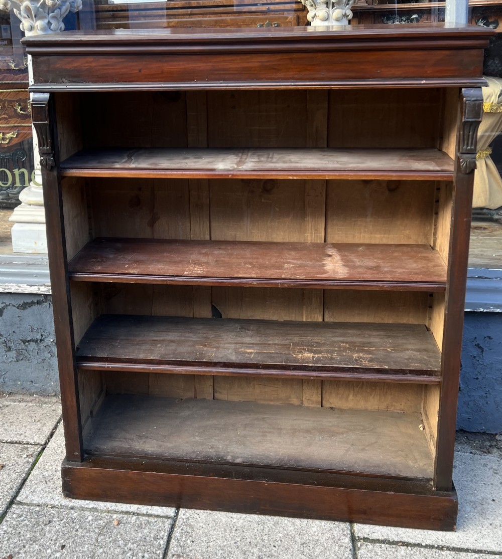 An Edwardian open walnut bookcase featuring four adjustable wooden shelves, side corbel carvings, and a solid plinth base.