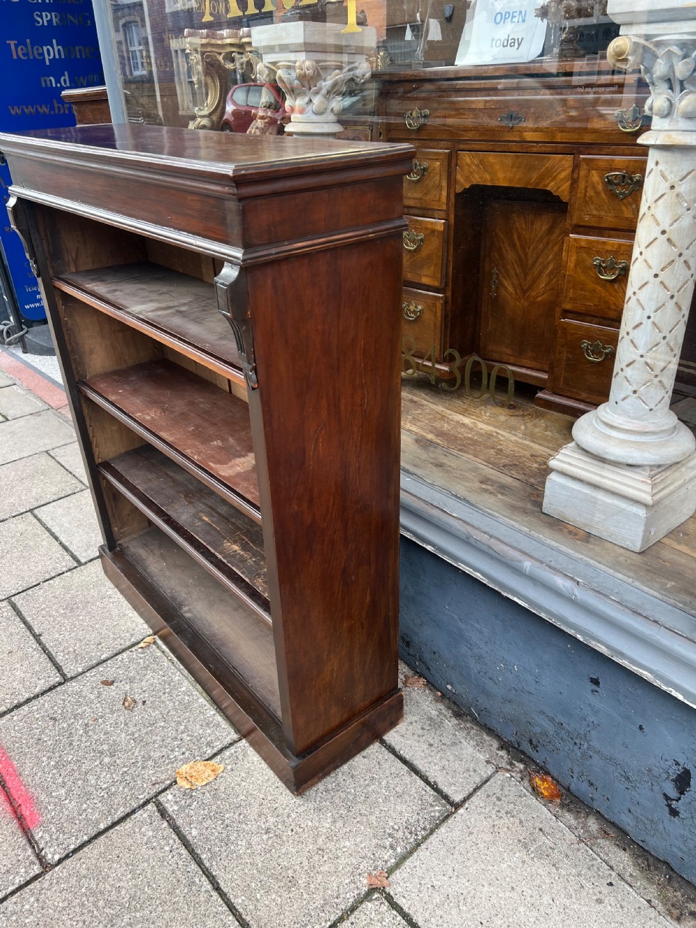 An Edwardian open walnut bookcase featuring four adjustable wooden shelves, side corbel carvings, and a solid plinth base. View X