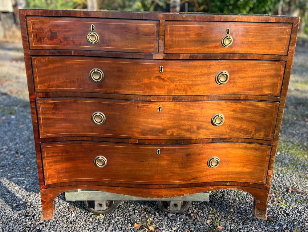 A George III mahogany chest of drawers featuring a serpentine front, line inlay, two short over three long drawers, and brass ring handles.