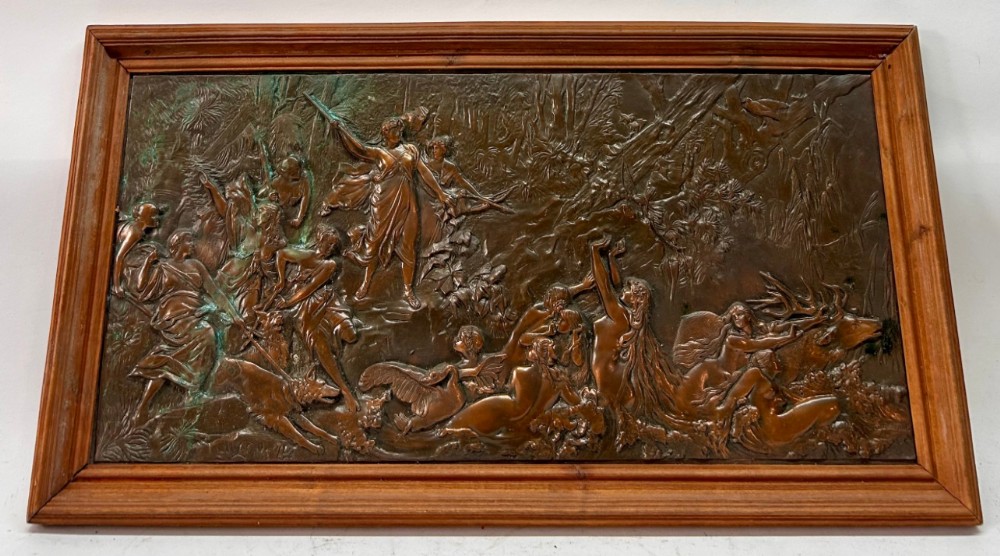 A rectangular framed bronzed copper relief plaque depicting Diana the Huntress surrounded by figures and hounds in a woodland setting.
