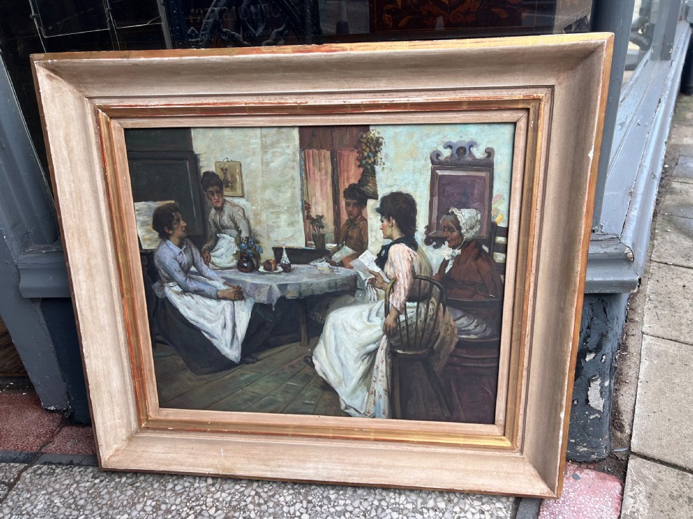 A framed oil on board painting depicting a group of people gathered indoors around a table in a domestic interior scene.