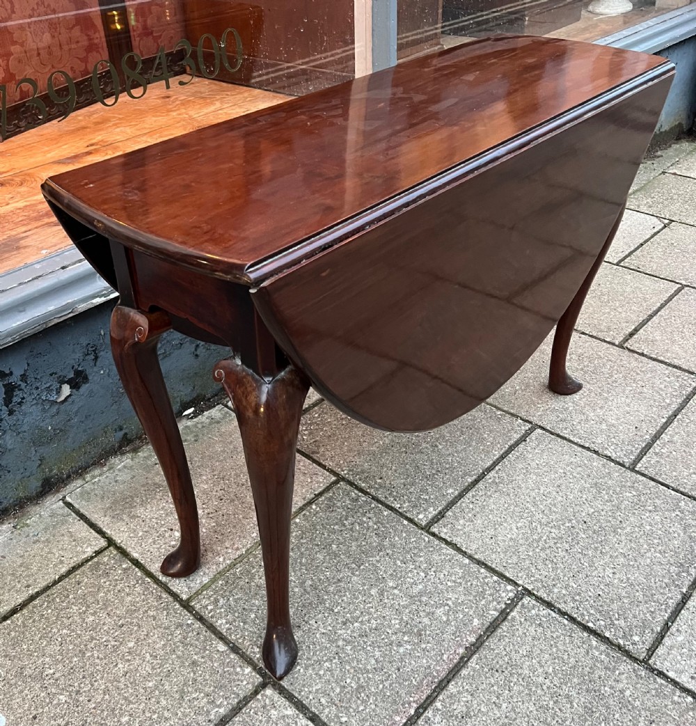An 18th-century Cuban mahogany drop leaf table with curved cabriole legs and carved pointed pad feet.