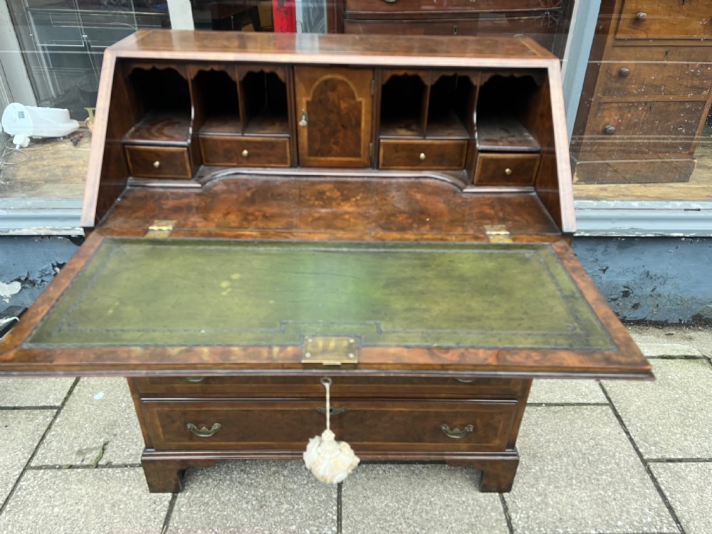 An 18th-century walnut and burr walnut slant-front bureau featuring crossbanded drawers, brass drop handles, and bracket feet. View V