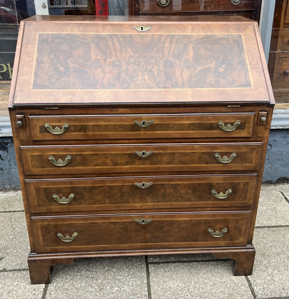 An 18th-century walnut and burr walnut slant-front bureau featuring crossbanded drawers, brass drop handles, and bracket feet.