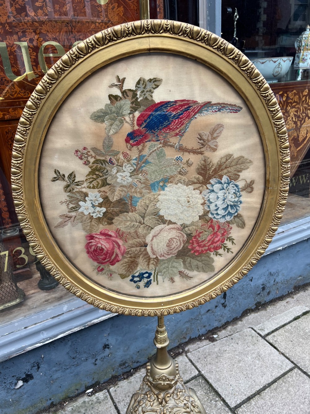 A 19th-century gilded pole screen with a tripod Rococo base framing an oval needlepoint panel depicting flowers and a bird. View X