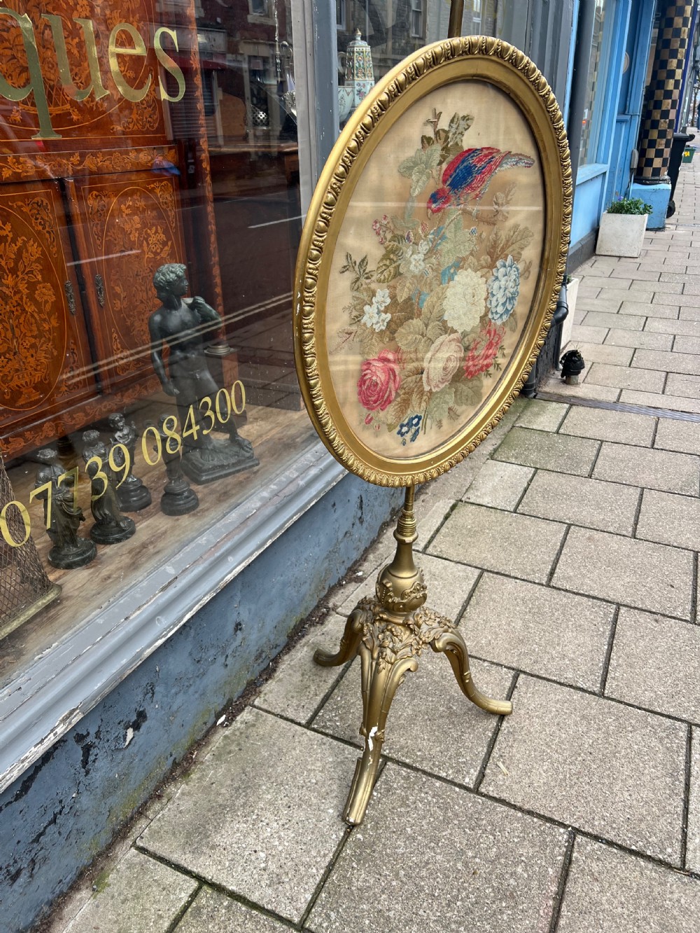 A 19th-century gilded pole screen with a tripod Rococo base framing an oval needlepoint panel depicting flowers and a bird. View XI