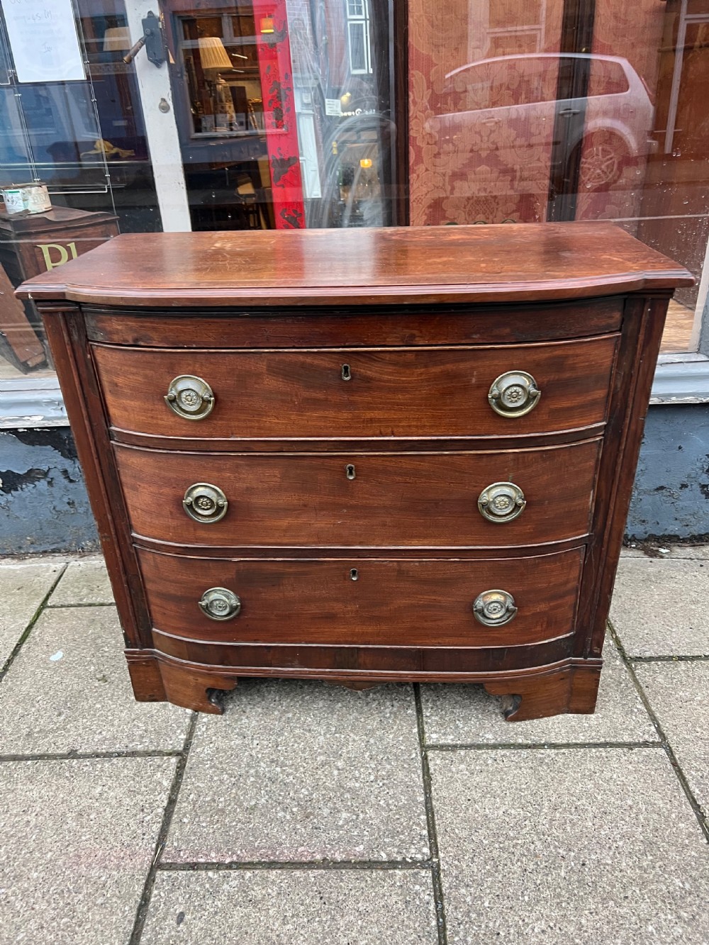 A small Georgian mahogany bow-front chest of three drawers featuring circular brass ring pulls and bracket feet.